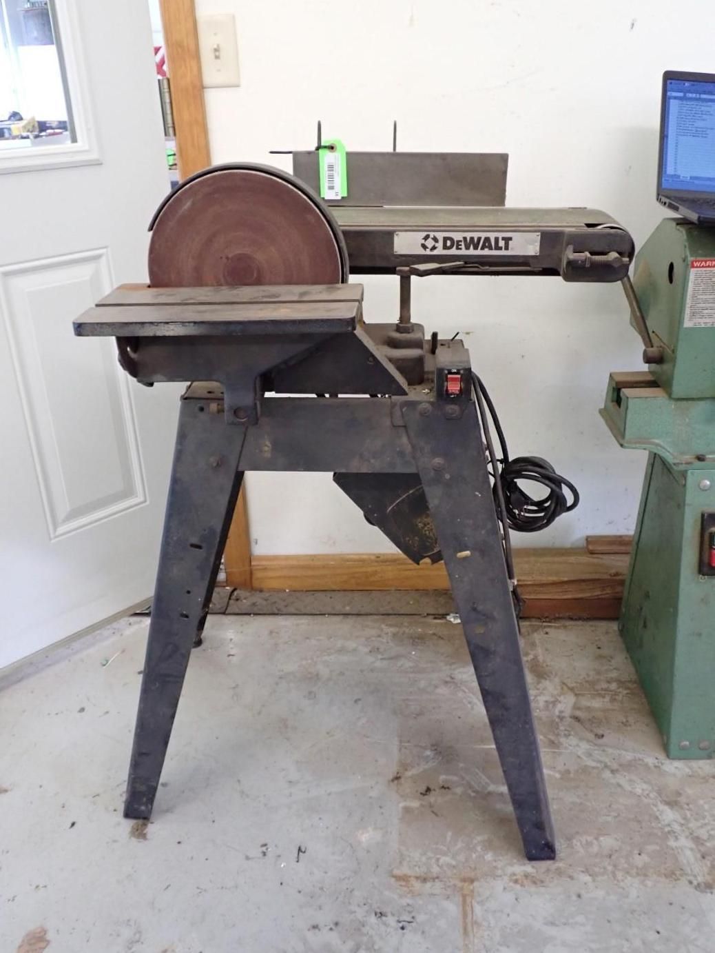 Black DeWalt disc and belt sander on a workshop floor, next to a lathe.