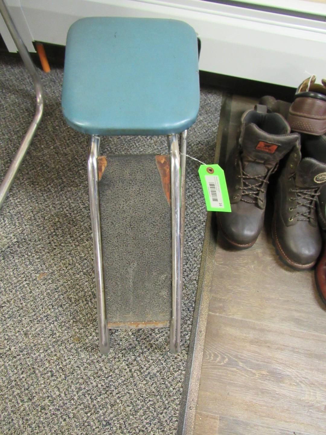 Blue square stool with chrome legs sits on gray carpet near boots.