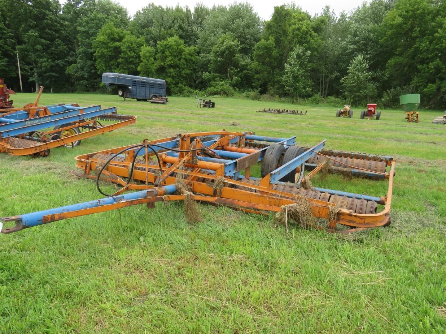 Orange and blue farm implement lying in a grassy field, trees in background.
