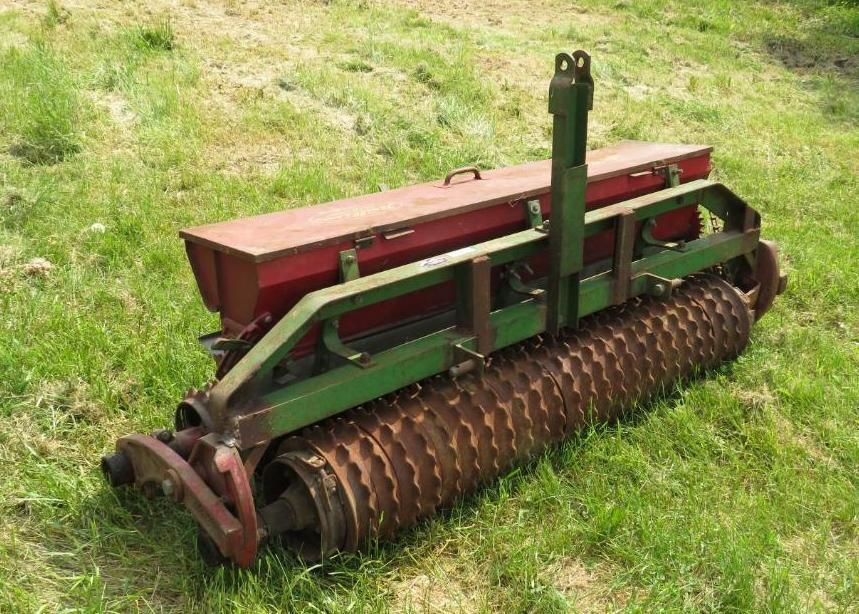 Green and red agricultural seeder on a grassy field.