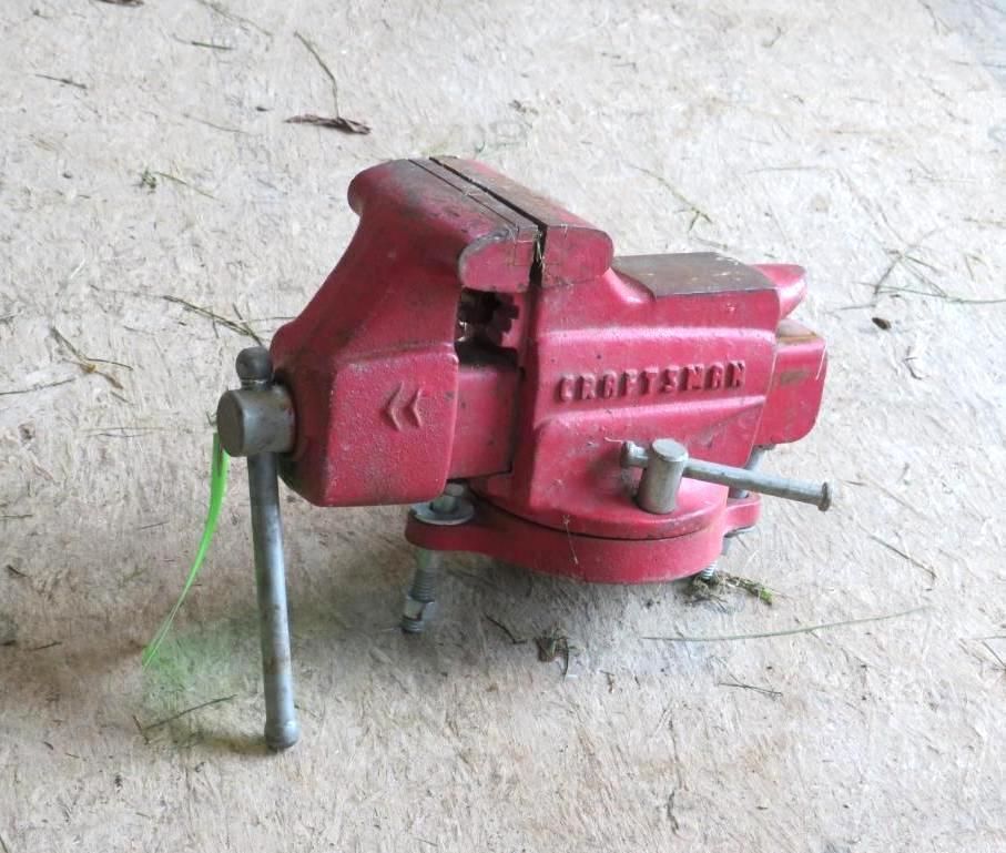 Red bench vise on a light-colored surface with a handle and jaw opening.