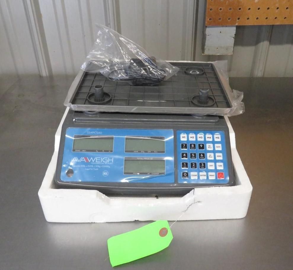 A digital scale with a dark gray base, black tray, and blue display screen, in a foam package, with a green tag.