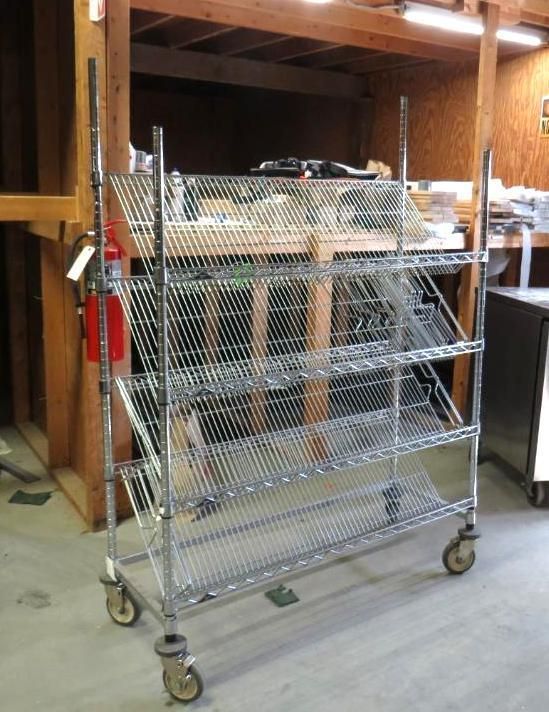 Metal shelving rack on wheels, leaning, with multiple wire shelves, indoors.
