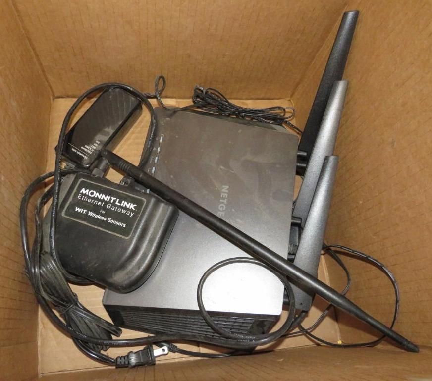 Box with a black Netgear router, antennas, and a black power adapter with wires.