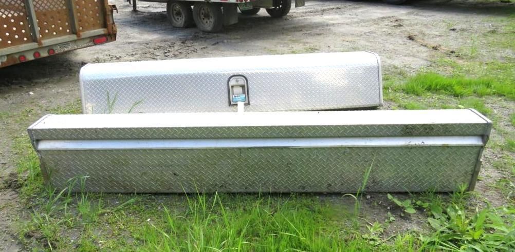 Two aluminum toolboxes on grass, with trailer in the background. One is longer, the other has a handle.