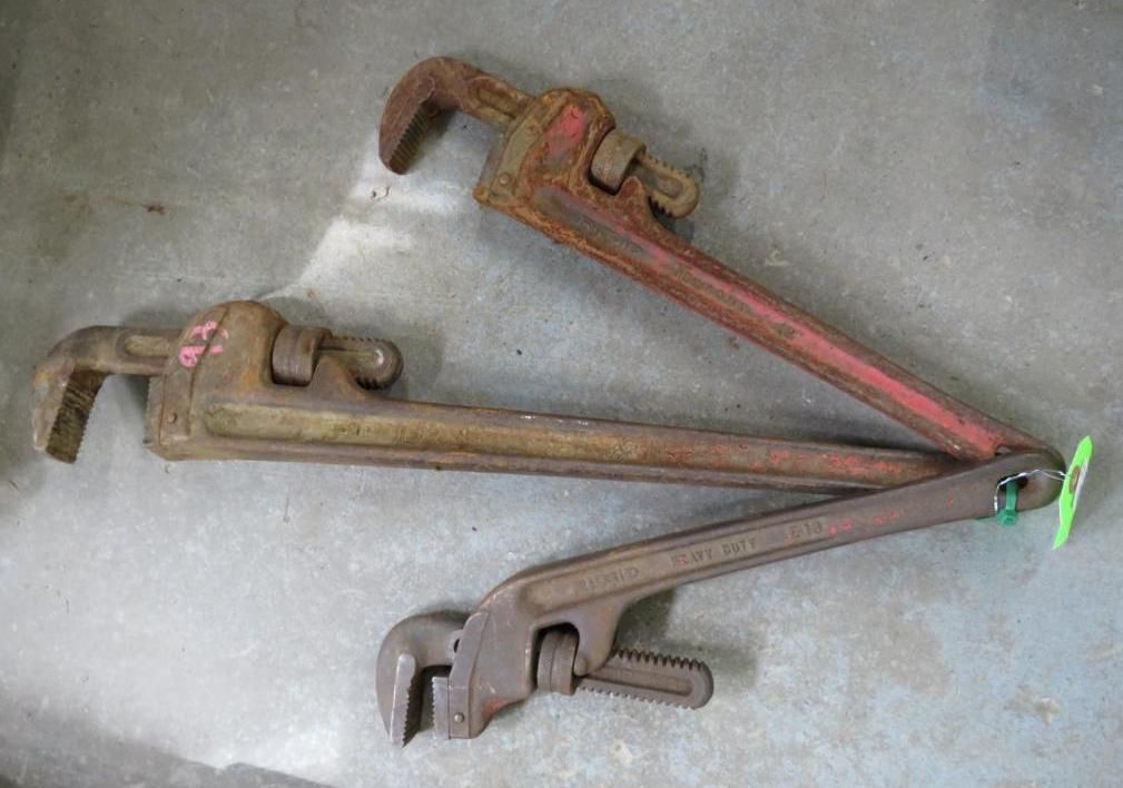 Three pipe wrenches of varying sizes laid on a concrete surface.