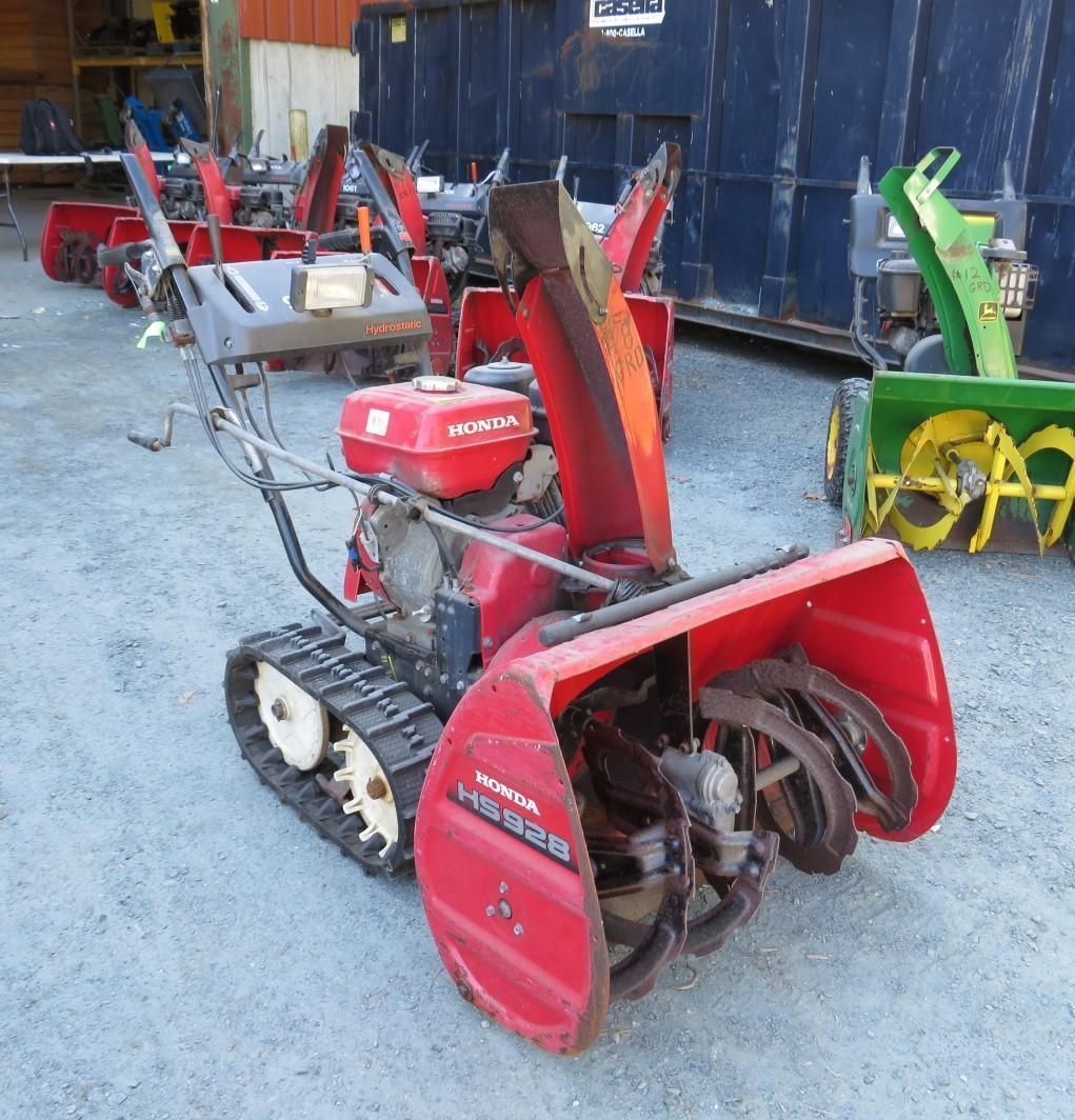 Red Honda snowblower with tracks, outdoors. Other snowblowers are in the background.