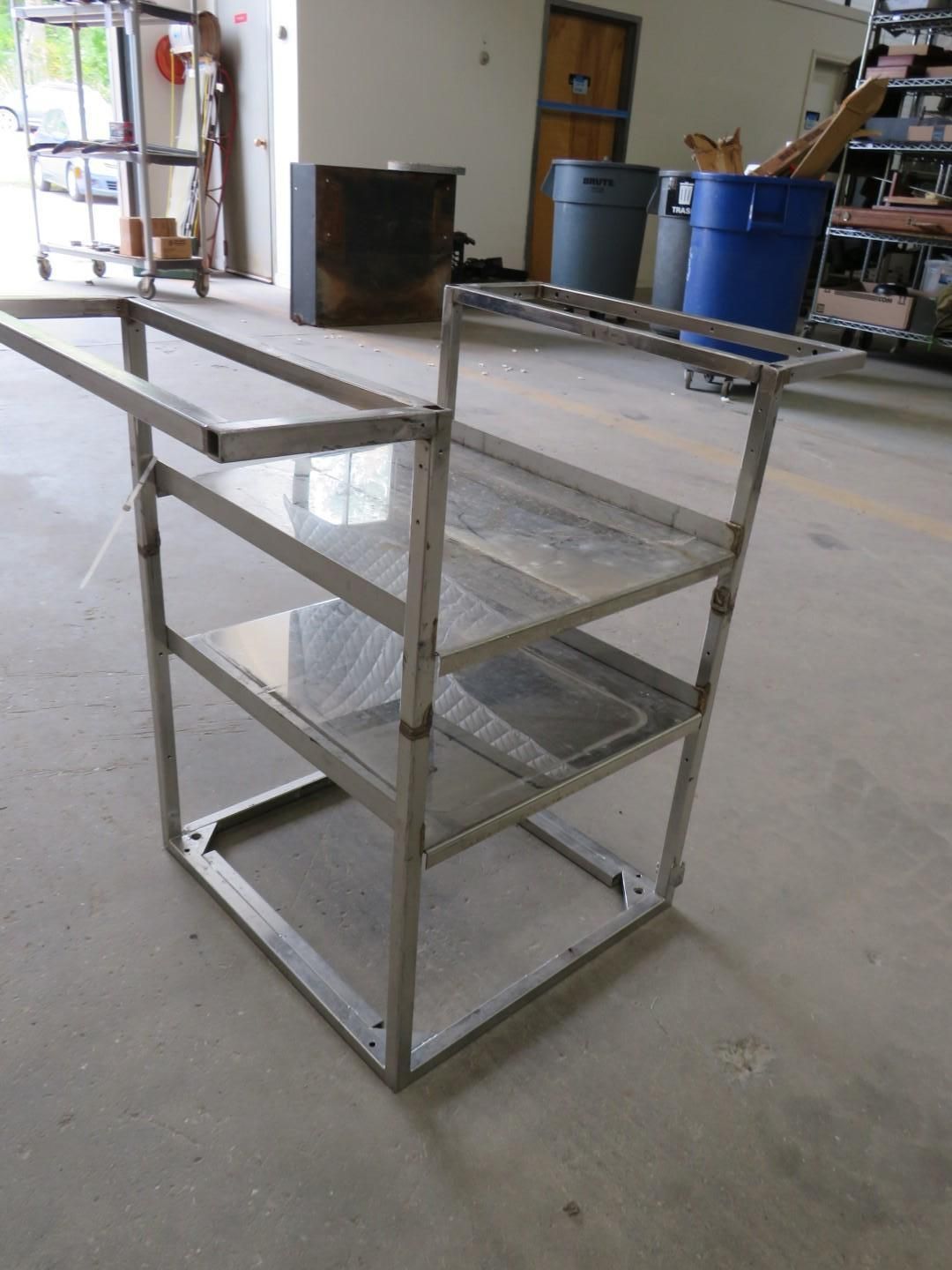 A three-tiered metal cart with an open top and shelves, in a workshop setting.