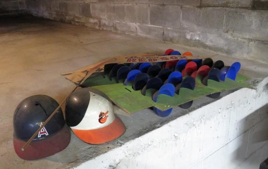 Baseball helmets and caps on a shelf in a concrete room. Blue, red, and orange colors are present.