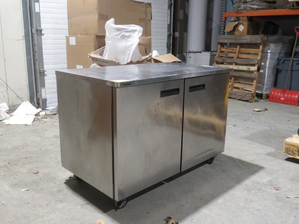 Stainless steel commercial under-counter refrigerator with two doors on wheels in a warehouse.
