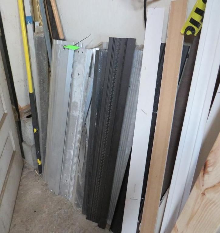 Pile of building materials against a wall, including metal, black, white, and wood planks.