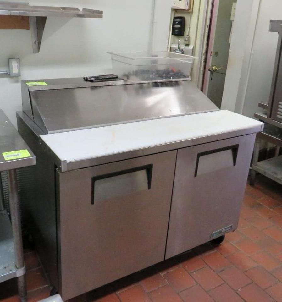 Stainless steel refrigerated food prep table with cutting board.