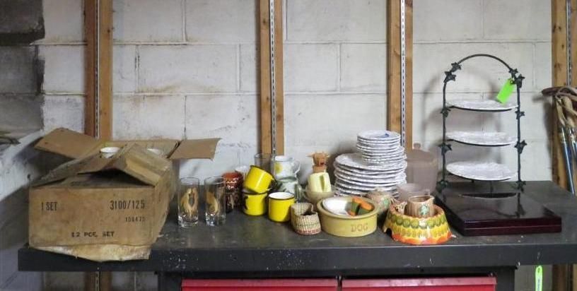 A table with dishes, cups, and a serving stand in front of a concrete block wall.