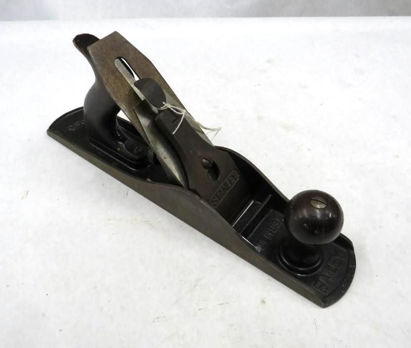 Dark hand plane with wooden handle and blade, resting on a white surface.