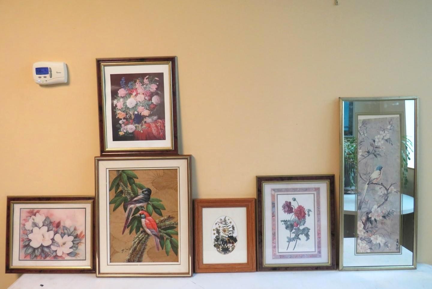 Framed floral and bird artwork on a beige wall, arranged on a white surface.