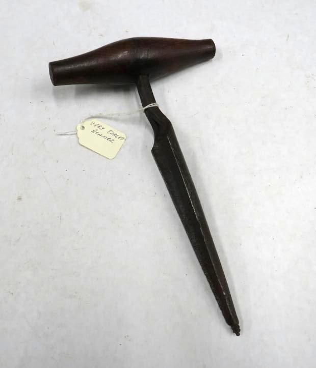 Dark-handled tapered tool with a long, pointed blade. A tag reads 