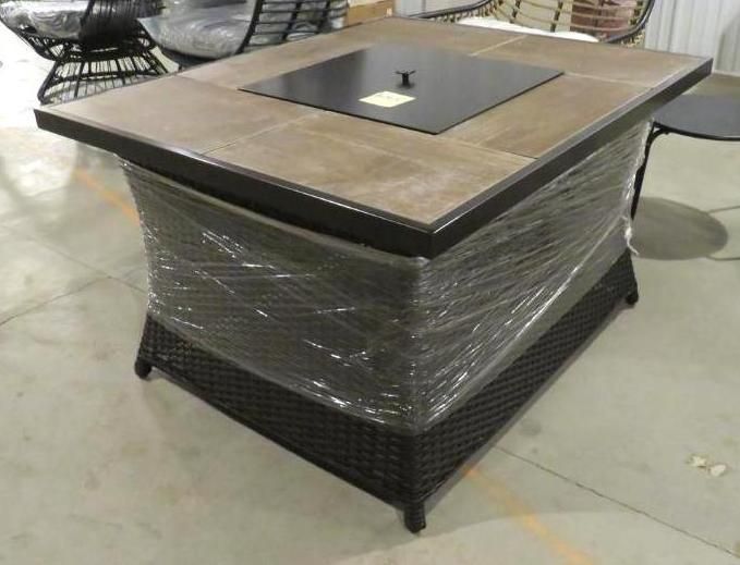 Square fire pit table with tiled top and woven base, wrapped in plastic.
