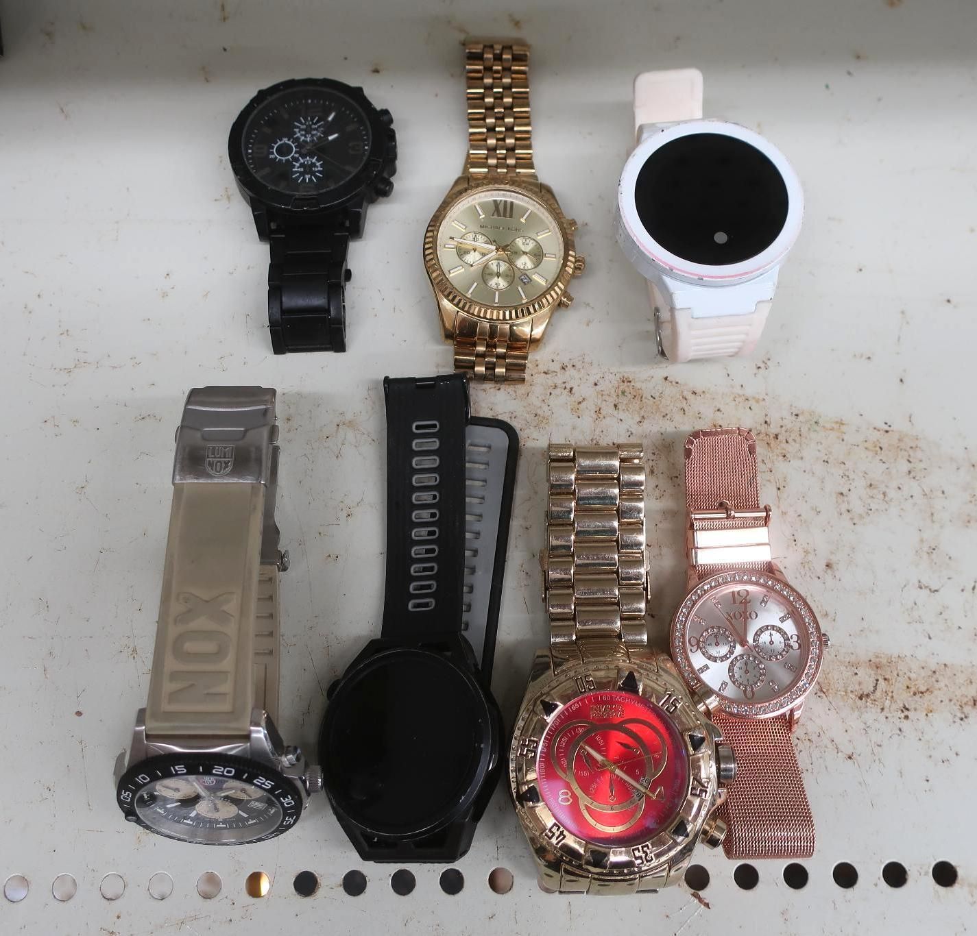 Seven wristwatches of various styles and colors on a light surface.