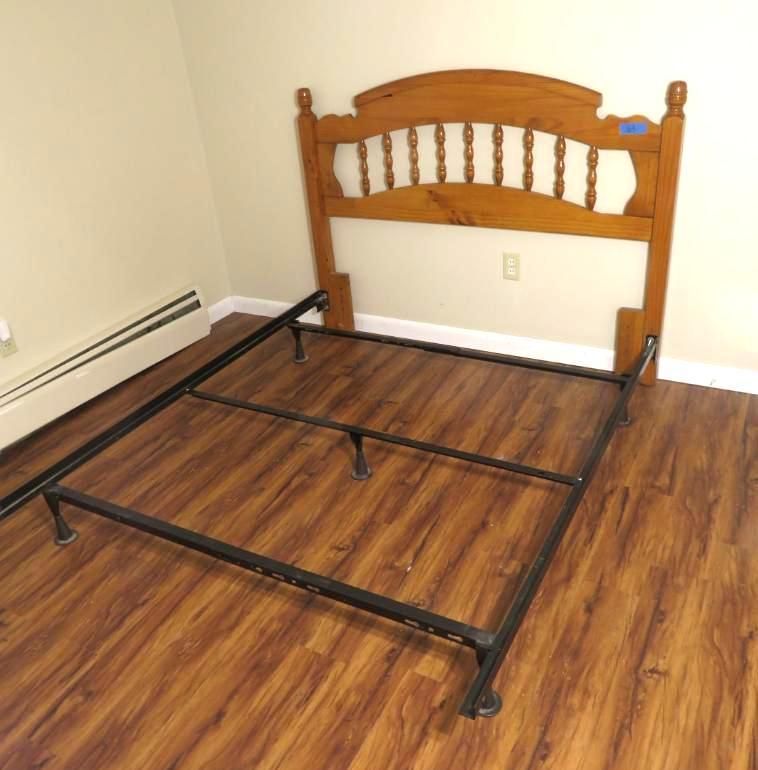 Wooden headboard next to a black metal bed frame on a wood floor in a room.