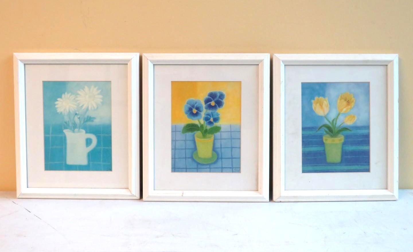 Three framed flower prints: white pitcher, blue pansies, and yellow tulips against blue and yellow backgrounds.