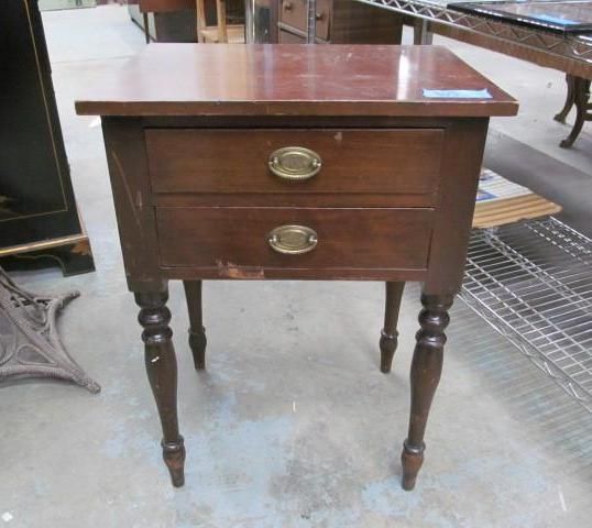 Wooden nightstand with two drawers and brass handles, set on turned legs.