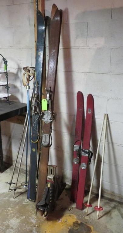 Three pairs of vintage skis and ski poles leaning against a white brick wall.