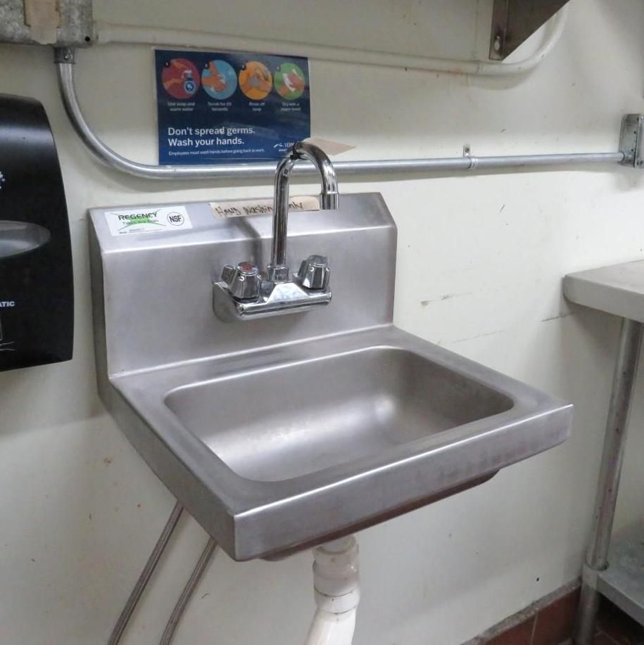 Stainless steel wall-mounted sink in a commercial kitchen with a faucet and water lines.
