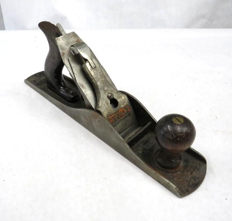 A metal hand plane with a wooden handle and knob, resting on a white surface.
