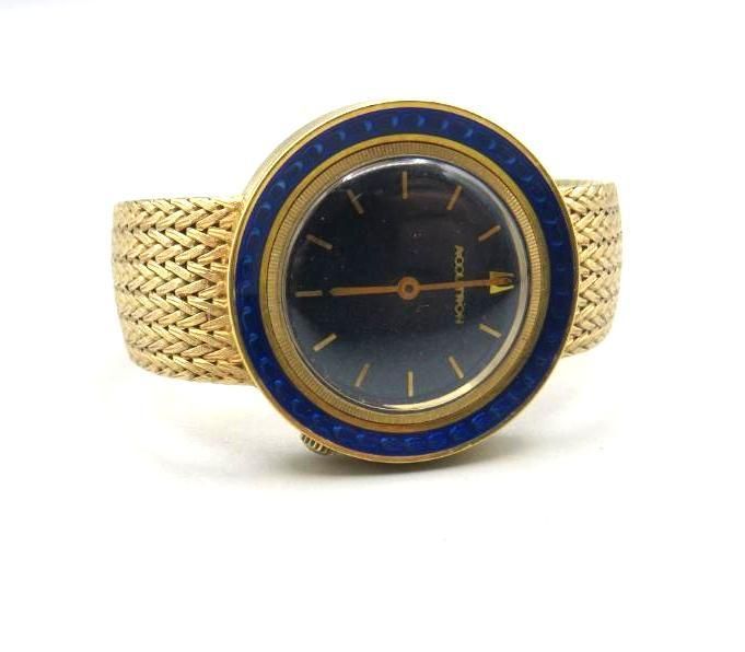 Gold wristwatch with a navy blue face, a gold bezel with a blue inlay, and a gold woven band.
