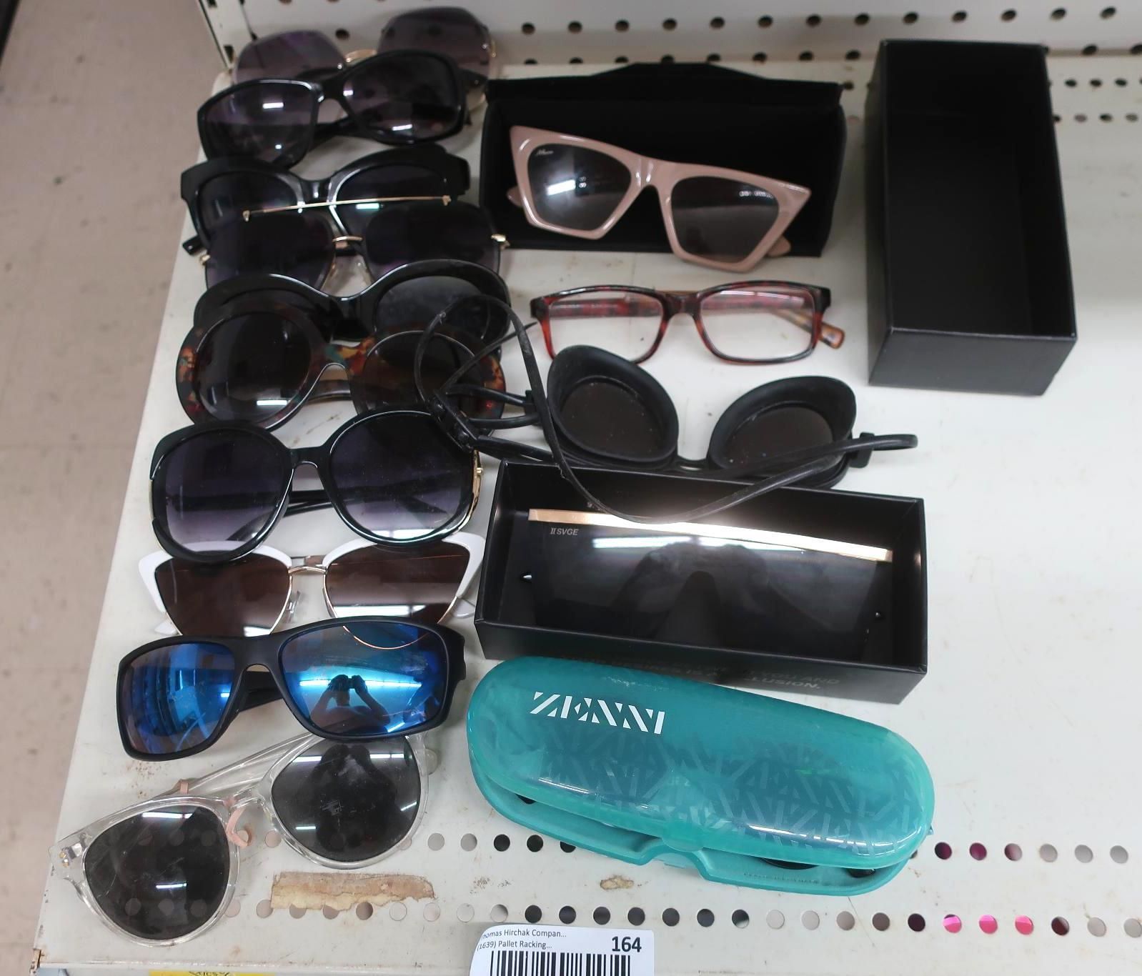 Sunglasses of various styles and colors arranged on a shelf, along with a glasses case.