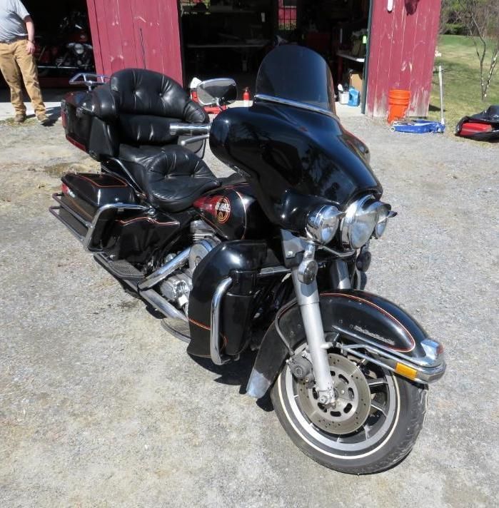 Black Harley-Davidson motorcycle parked on a gravel surface in front of a red building with an open door.