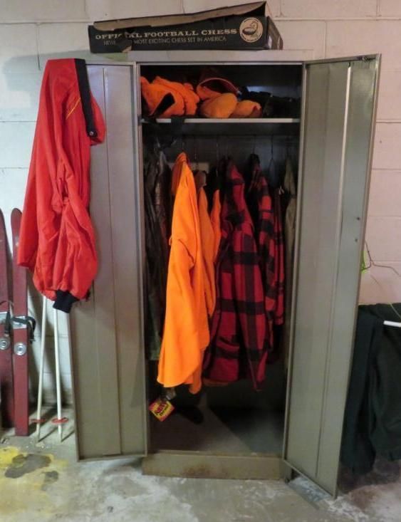 Metal locker open, displaying orange and plaid hunting gear, with red jacket hanging outside.