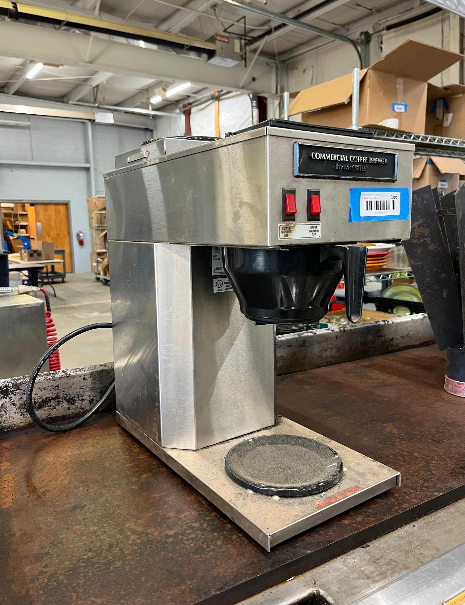Stainless steel commercial coffee maker on a rusty surface.