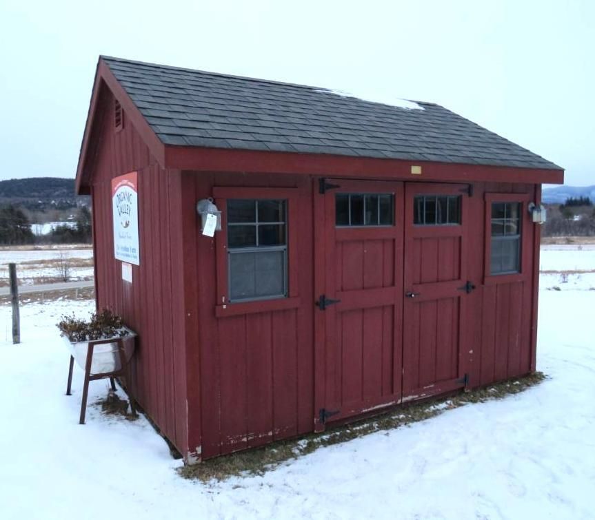 Red wooden shed with dark roof, windows, and double doors in a snowy field.