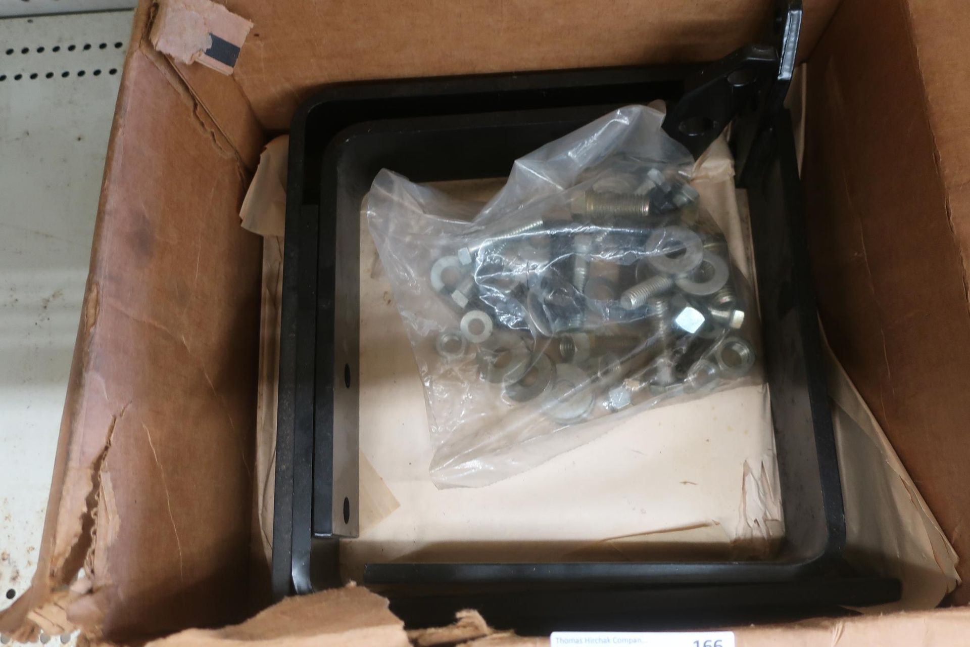Black rectangular part and hardware inside a cardboard box.