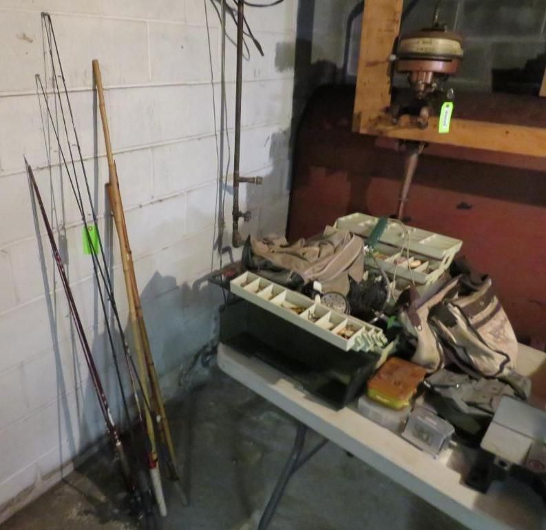 Fishing rods leaning against a wall, fishing tackle and an outboard motor on a folding table.