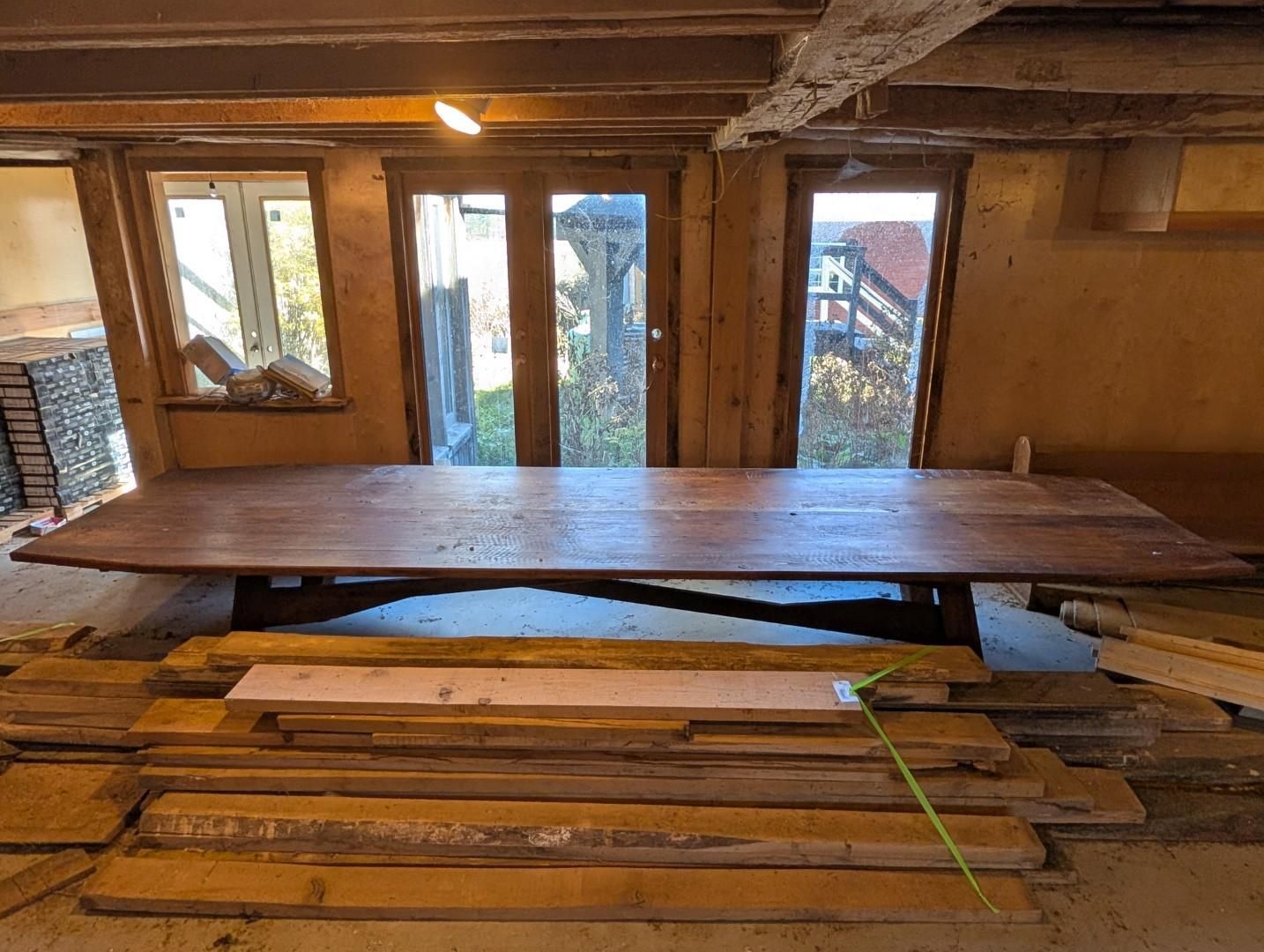 Partially built wooden interior with a large table, exposed beams, and windows in the back wall
