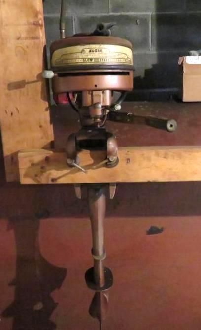 Antique bronze outboard motor, mounted on wooden supports, with propeller visible.