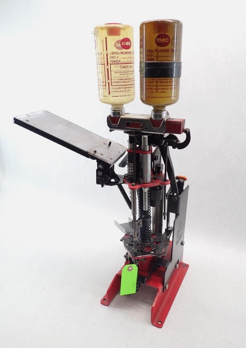 Red and silver reloading press with two powder dispensers, on a white surface.