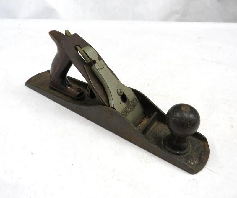 A dark-colored hand plane with wooden handles and a metal blade, resting on a white surface.
