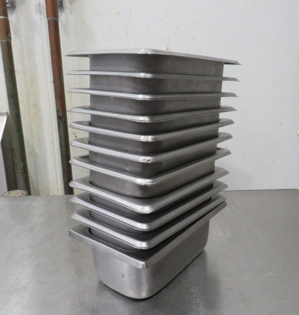 Stack of stainless steel food storage pans on a metal surface.