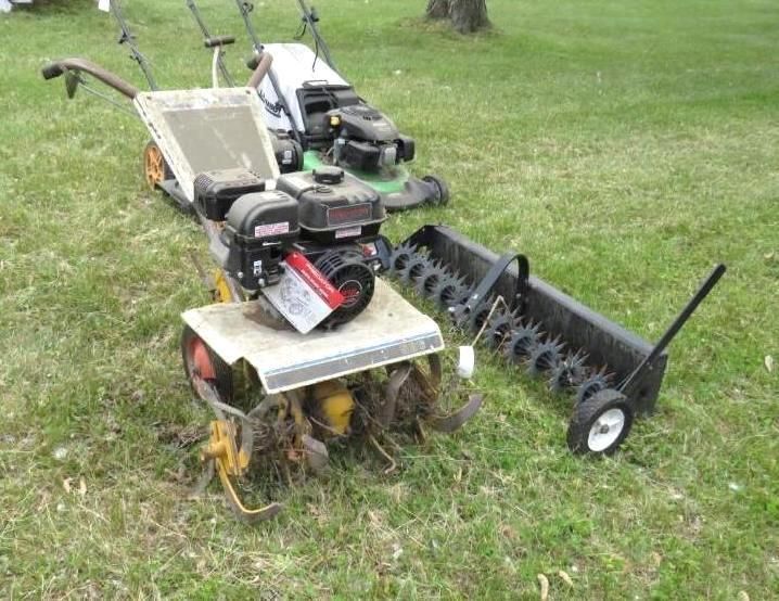 A tiller, lawn aerator, and lawnmower on grass.