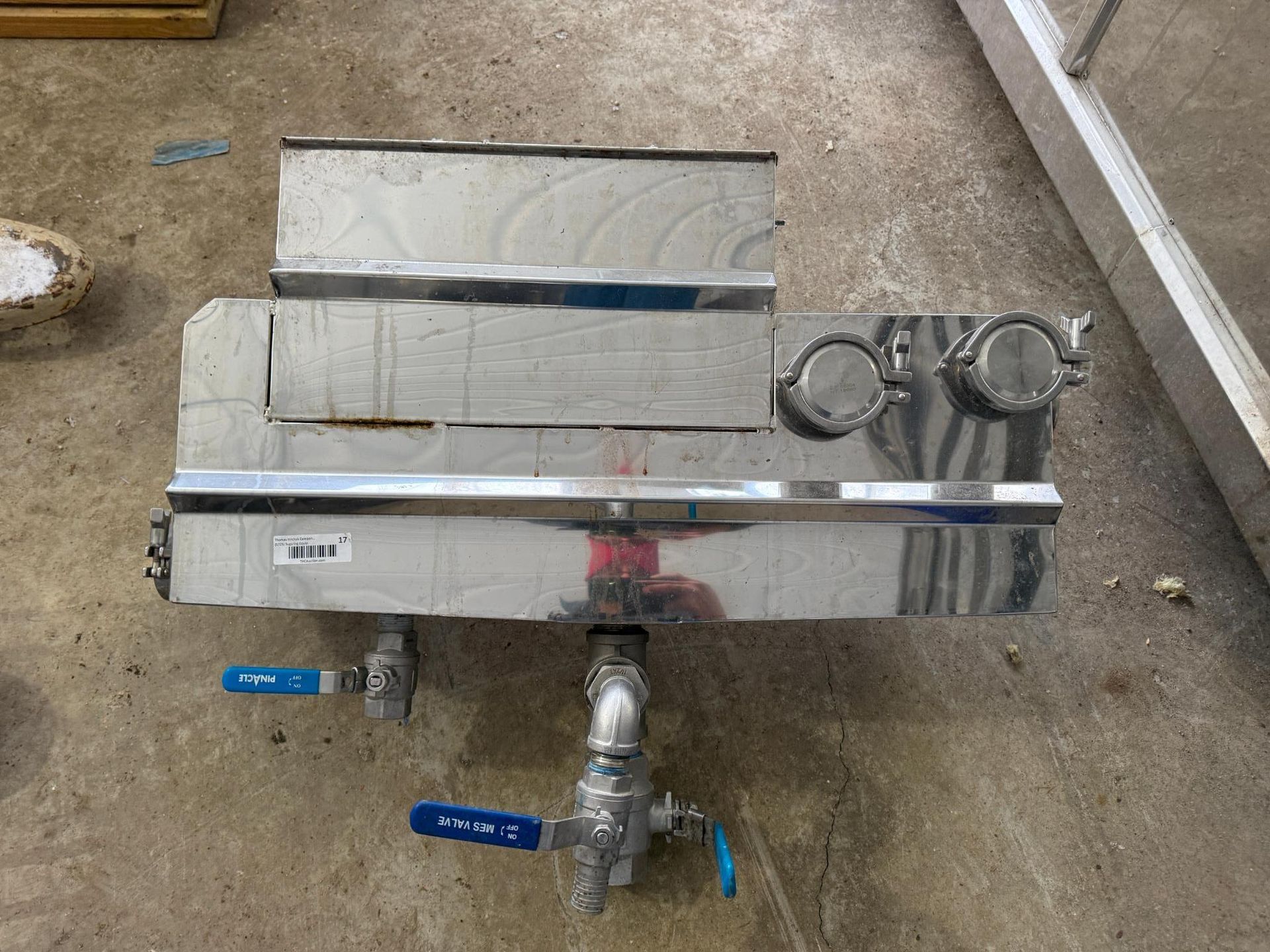 Stainless steel industrial machine with valves and fittings on a concrete floor.