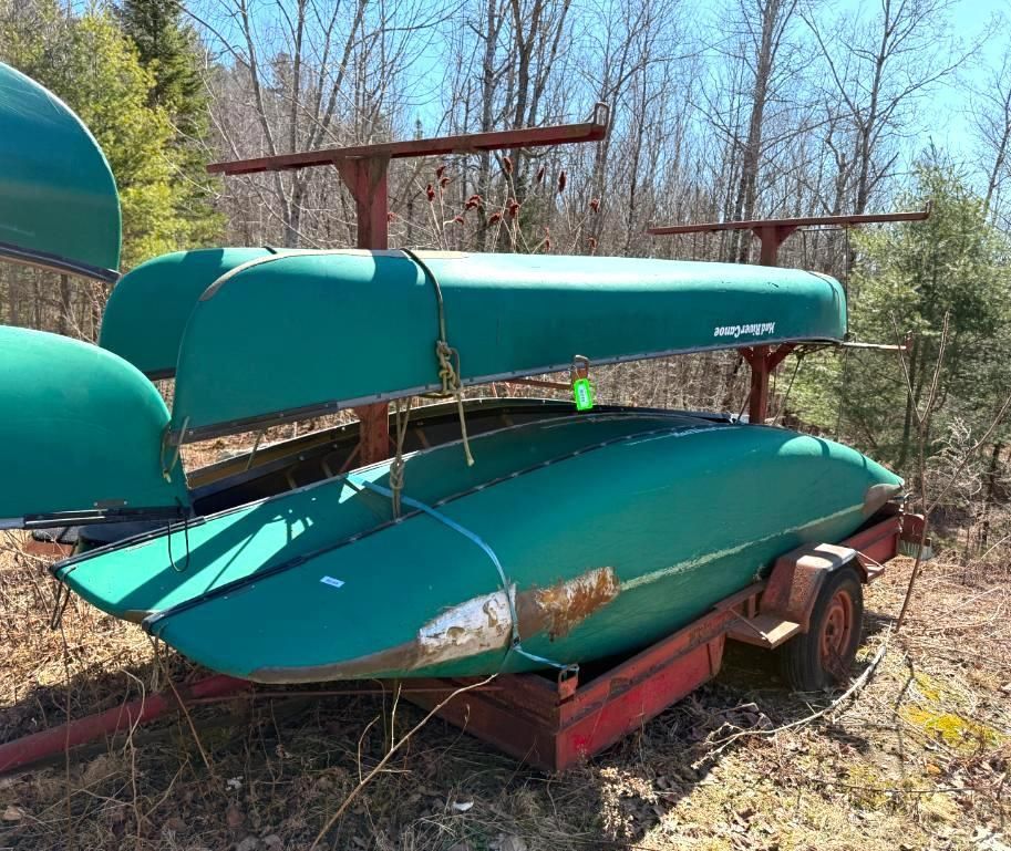 Green canoes stacked on a red trailer, outdoors.