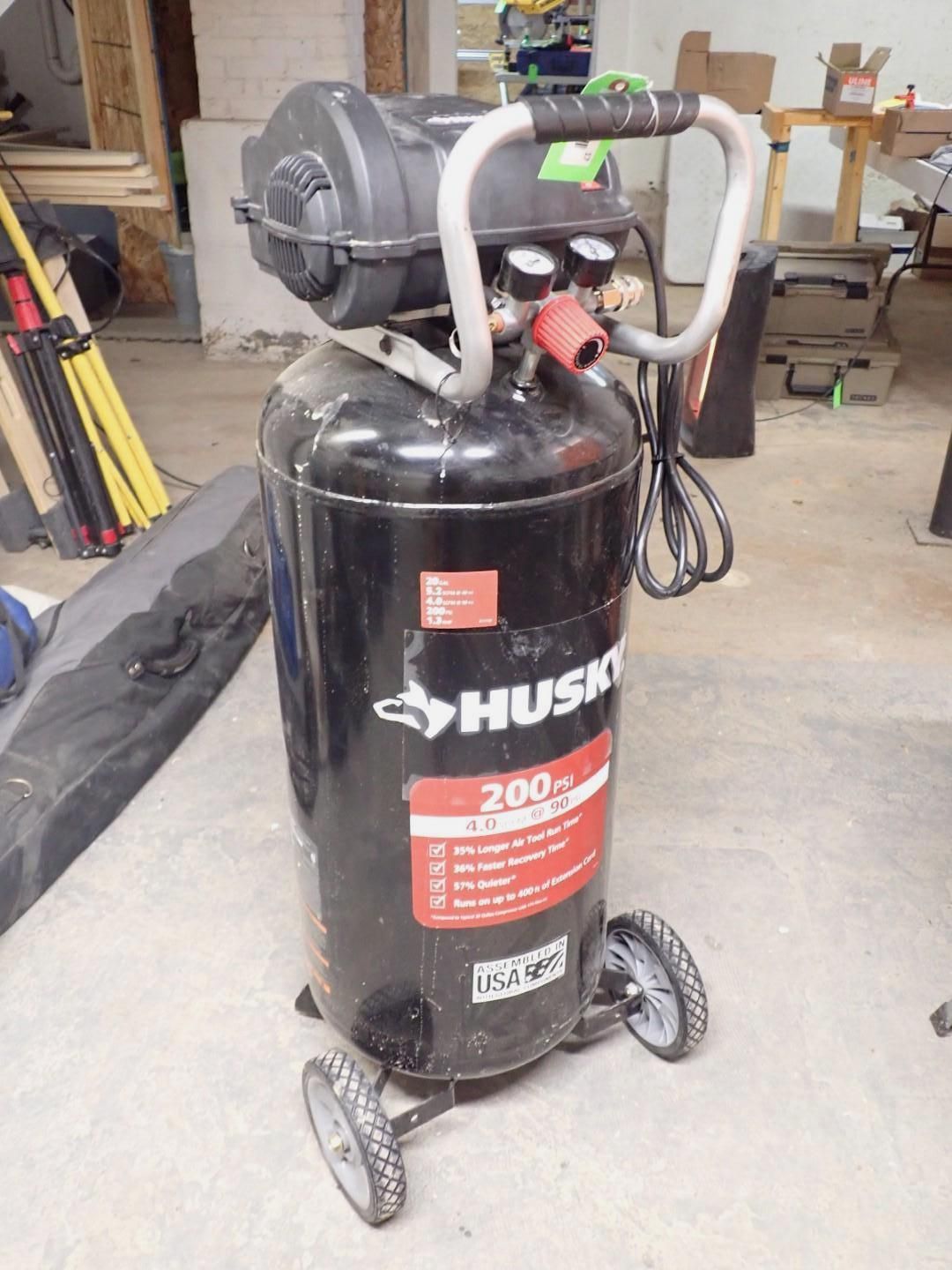 Black Husky 20-gallon air compressor with gauges and a handle, on wheels, indoors.