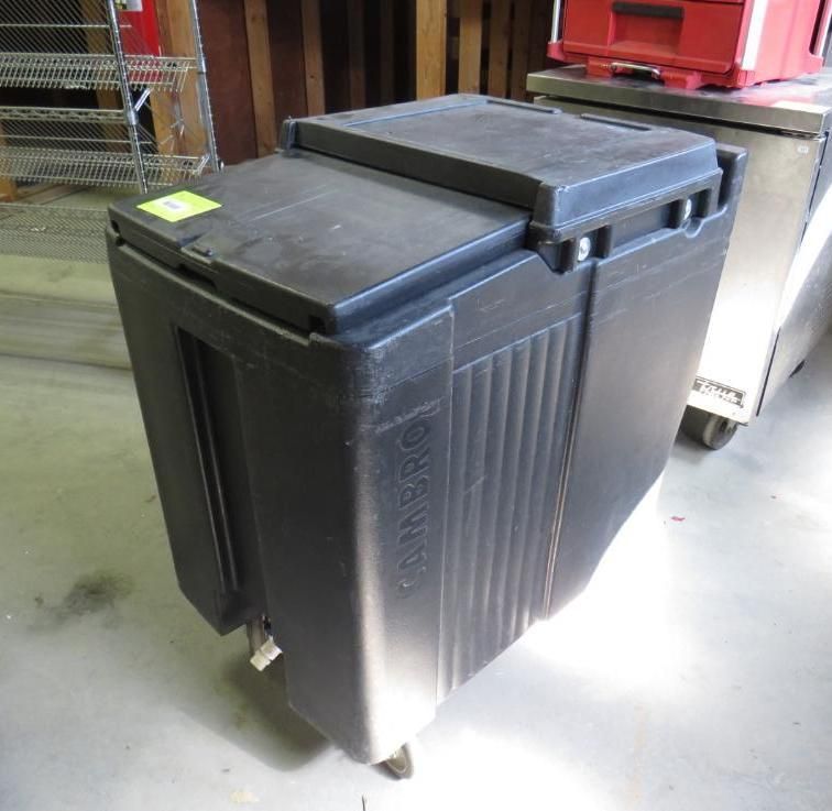 Black food transport container on wheels, in a kitchen or storage area.