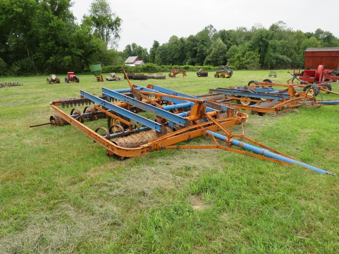 Orange and blue farm rake on green grass.
