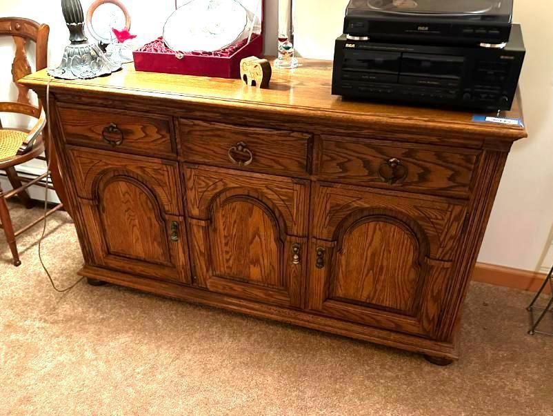 Wooden cabinet with three drawers and doors, holding a turntable and decor on top.