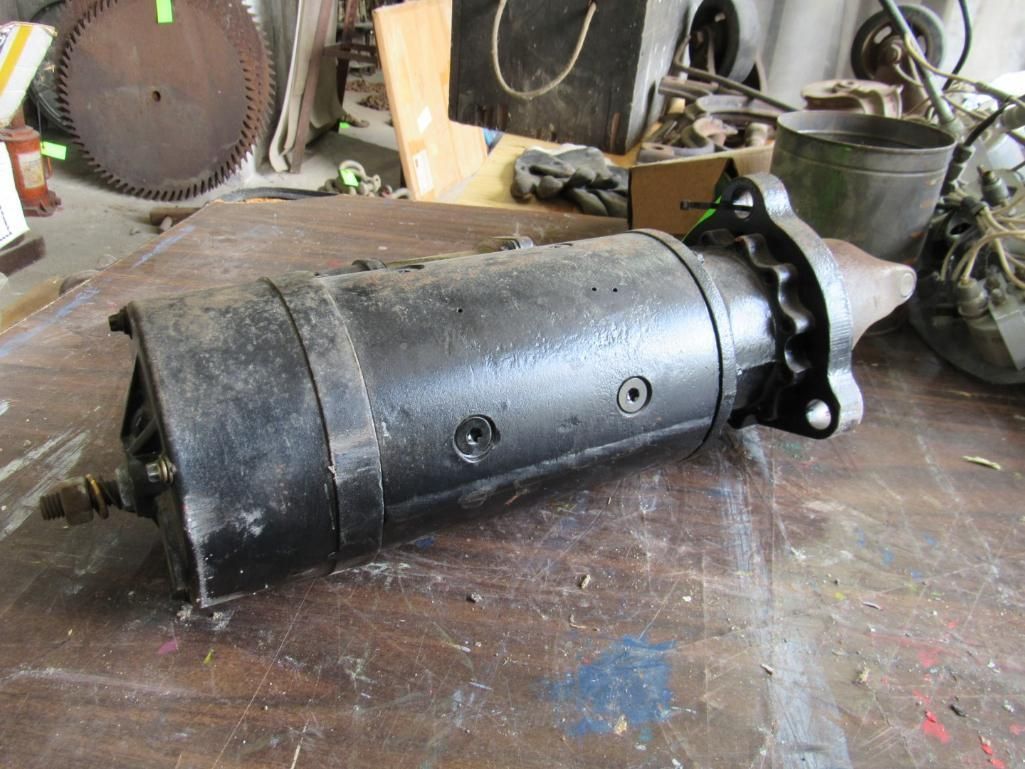 Black electric starter motor on a wooden surface, with other tools and parts in the background.