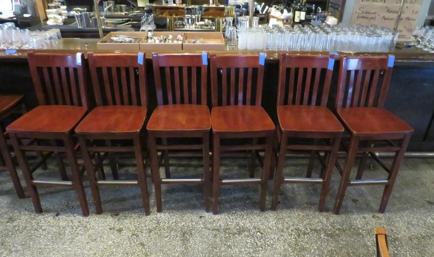 Six dark wooden bar stools in a row.